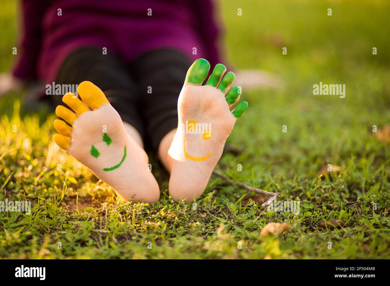 Bambina con piede dipinto su erba verde divertirsi all'aperto nel parco primaverile. Foto Stock