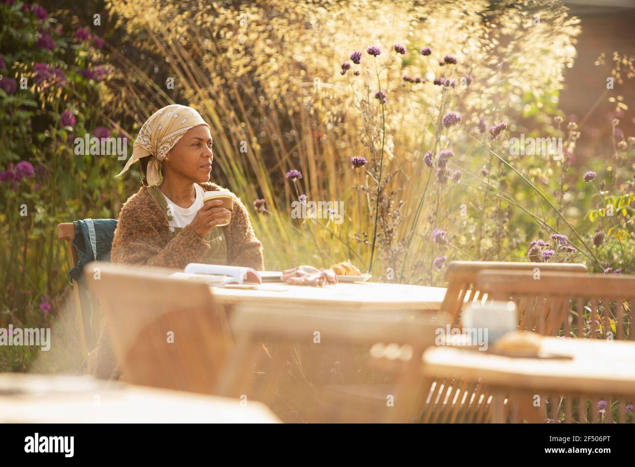 Donna con caffè al soleggiato tavolo da caffè giardino idilliaco Foto Stock
