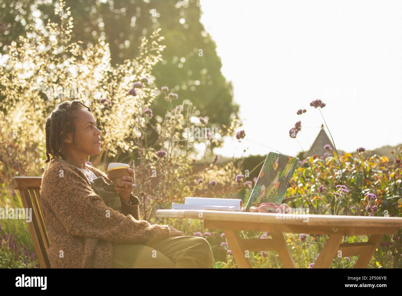 Donna serena con caffè che lavora a tavola in idilliaco sole giardino Foto Stock