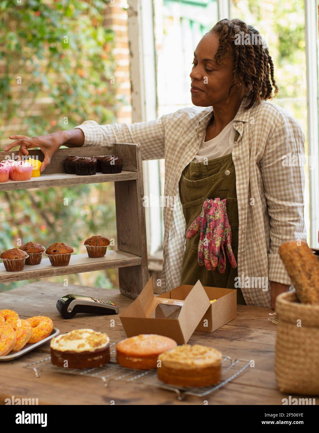 Panettiere femminile che dispone i cupcakes sul ripiano di esposizione in negozio Foto Stock