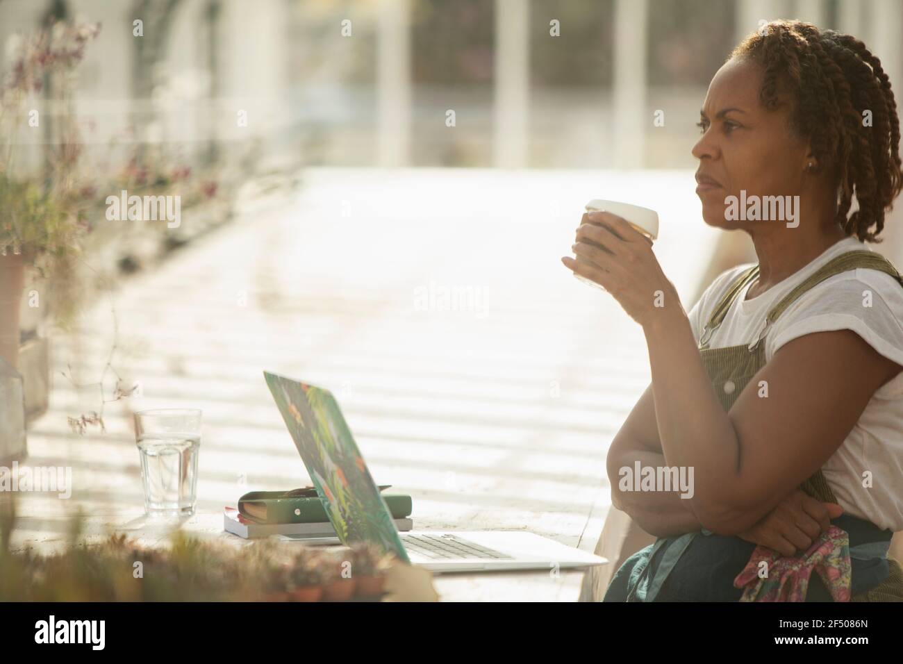 Donna proprietario del centro giardino bere caffè in serra soleggiata Foto Stock