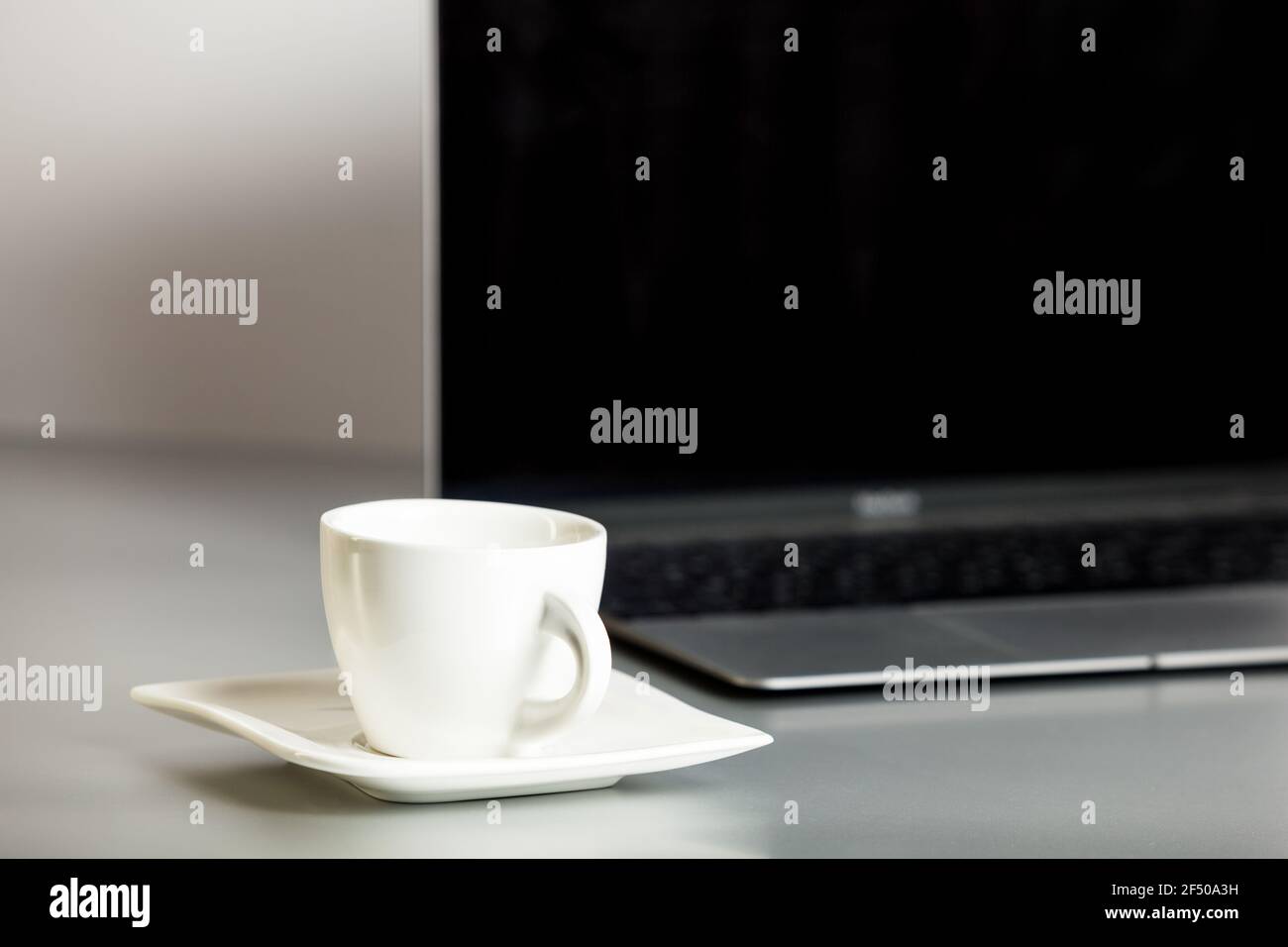 Ha aperto il laptop e la tazza di caffè sul piatto in primo piano sul tavolo grigio e sfondo bianco. Postazione di lavoro remota, ufficio domestico. Comunicazione online. Foto Stock