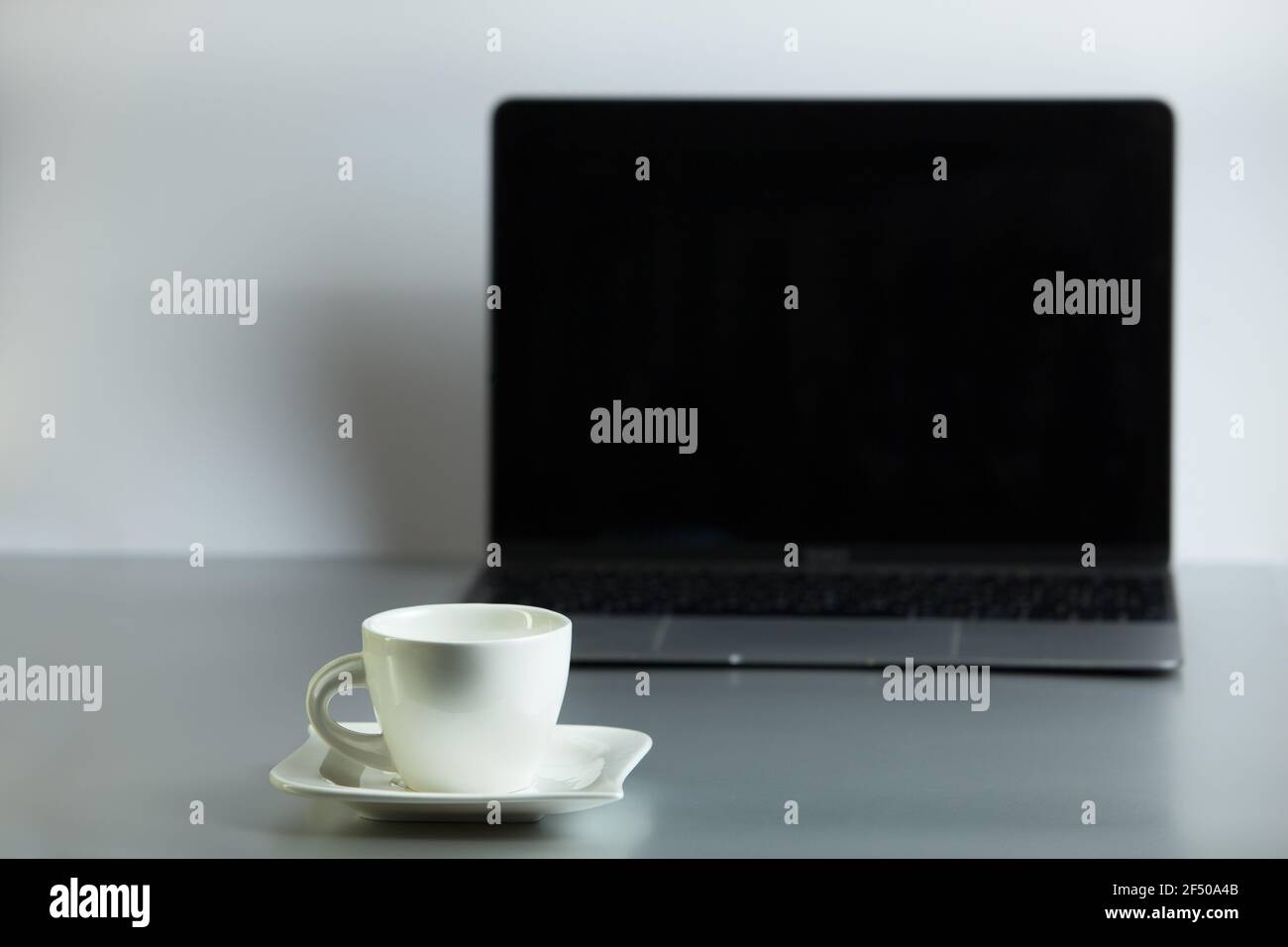 Composizione con un moderno laptop aperto una tazza di caffè bianca e un piatto sul tavolo su uno sfondo grigio chiaro. Postazione di lavoro remota, lavoro da casa. Foto Stock