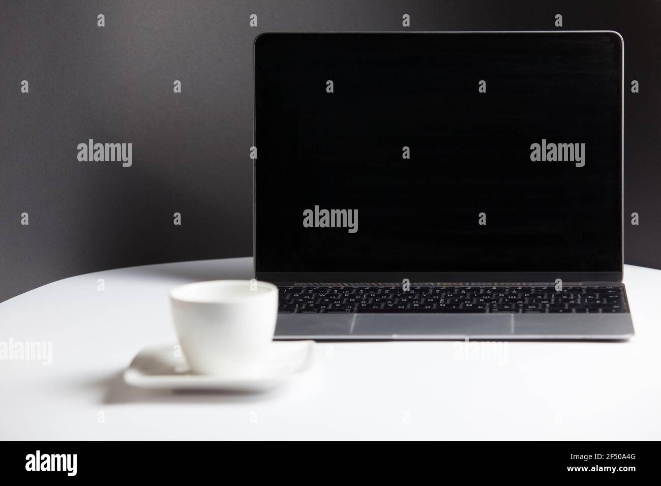 Composizione con un moderno laptop aperto e una tazza di caffè con piatto sul tavolo bianco su sfondo grigio. Postazione di lavoro remota, ufficio domestico. Foto Stock