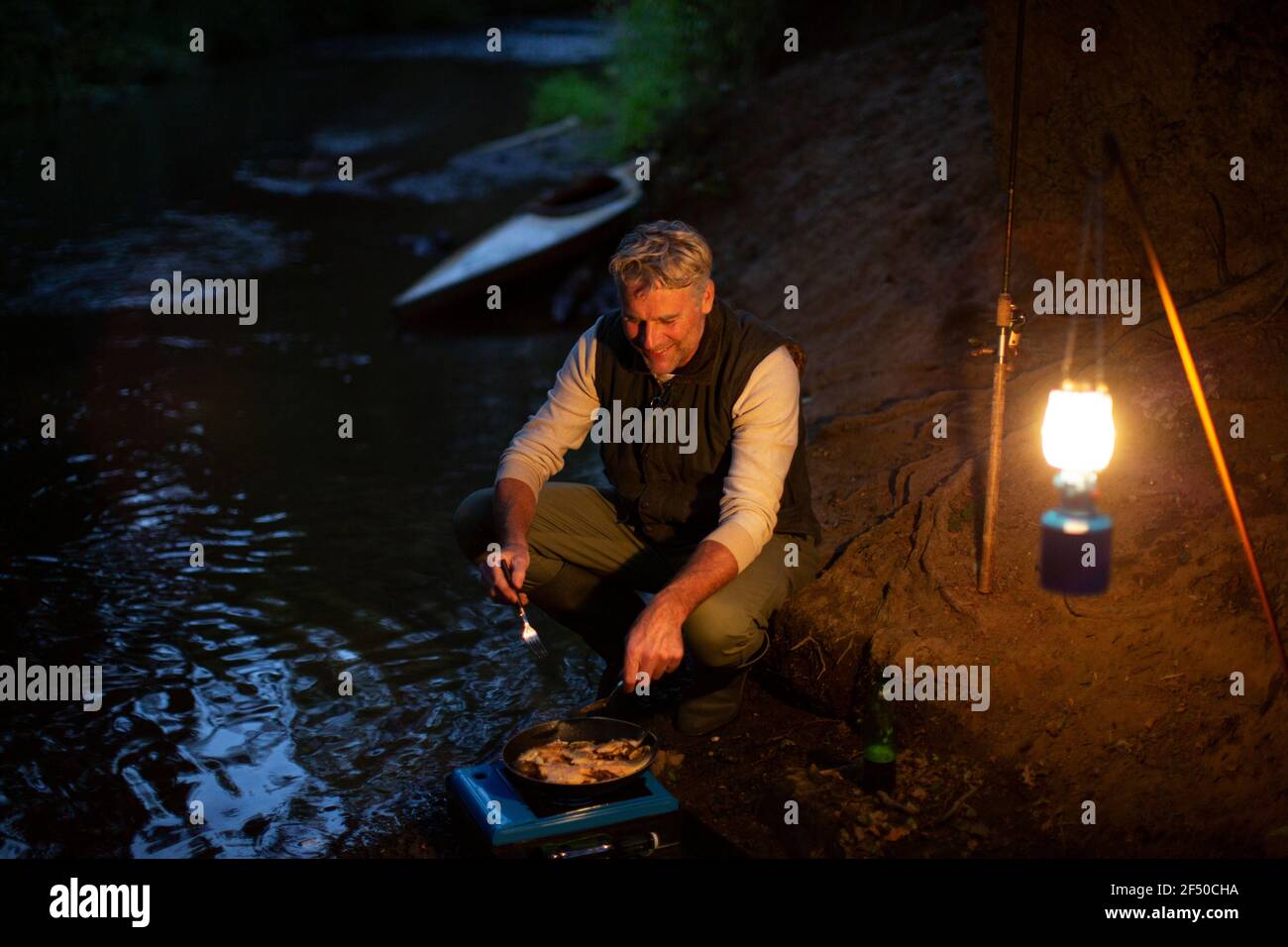 Pescatore maschio che cucinano pesce fresco catturato su stufa da campeggio a. notte Foto Stock
