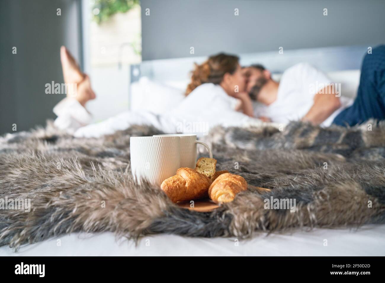 Una coppia affettuosa che si bacia sul letto dietro il croissant e la tazza di caffè Foto Stock