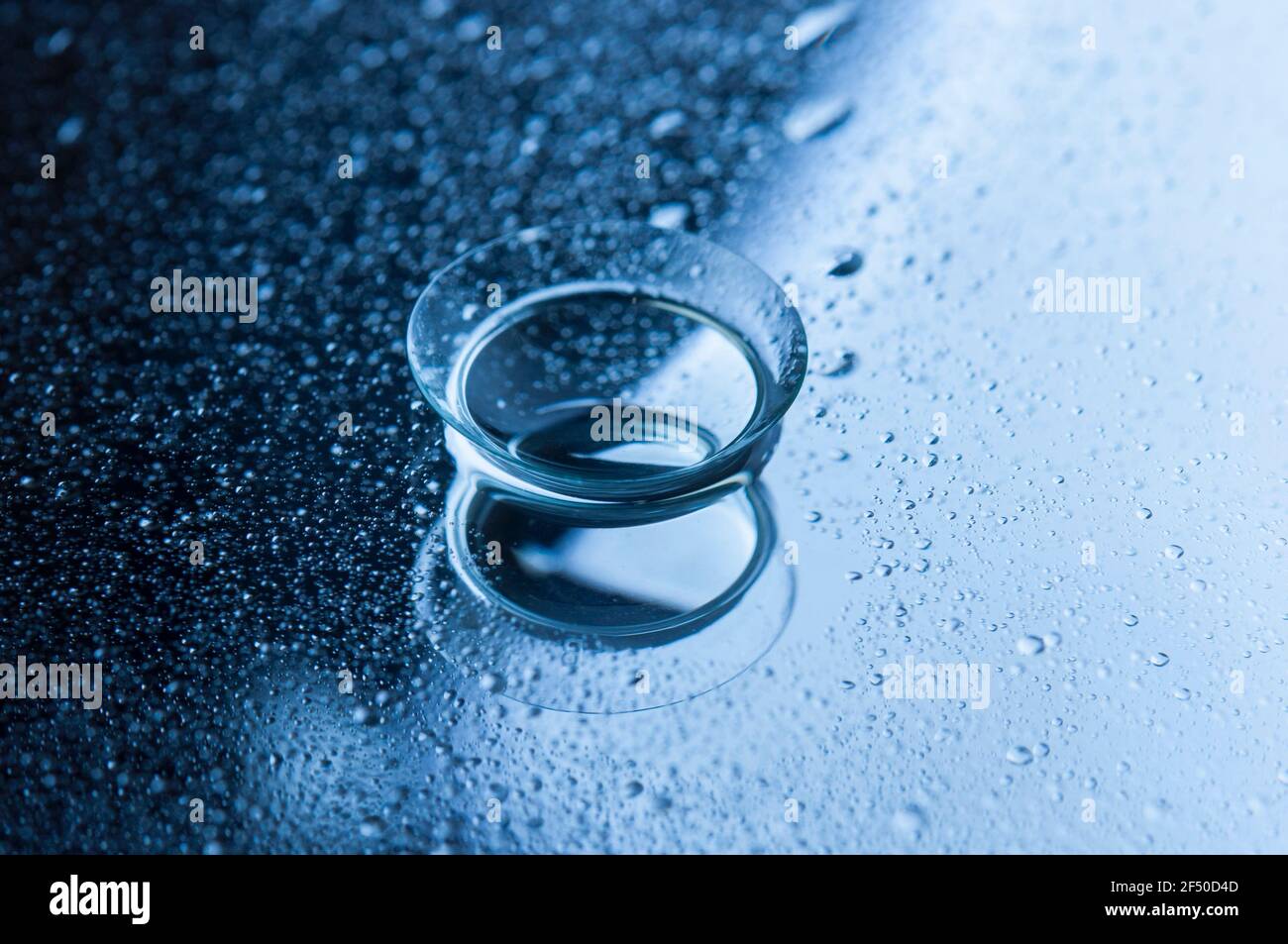 Lente a contatto con gocce d'acqua su uno sfondo a specchio. Immagine con tonalità blu. Vista concettuale. Foto Stock