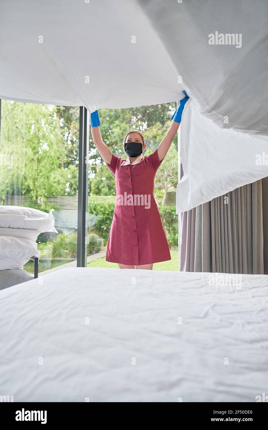 Cameriera dell'hotel femminile in maschera facciale che fa il letto in hotel camera Foto Stock