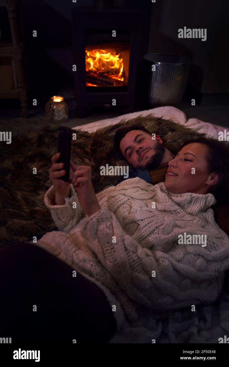 Una coppia romantica che usa uno smartphone all'accogliente caminetto Foto Stock