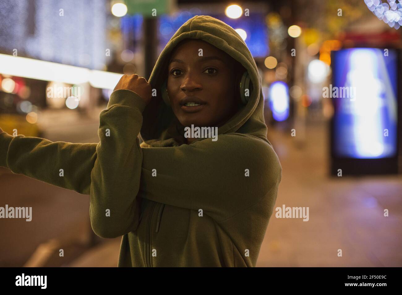 Giovane corridore femminile in stretching hoody sul marciapiede della città a. notte Foto Stock