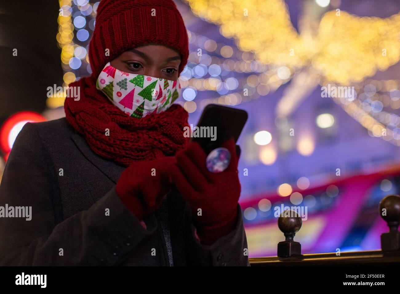 Giovane donna in maschera di Natale e sciarpa con smart telefono Foto Stock