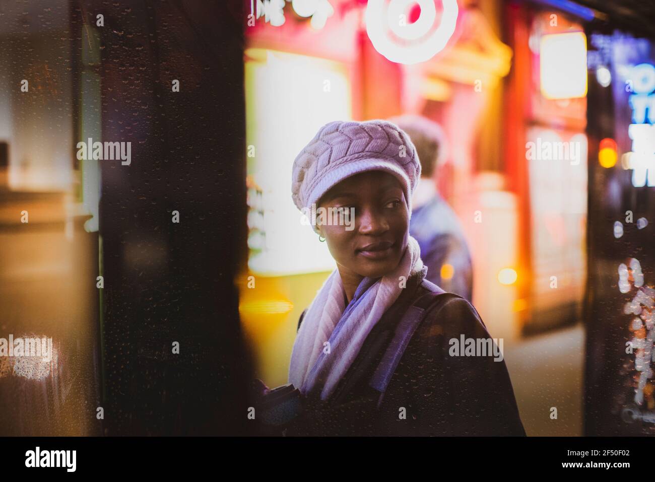 Giovane donna in cappello che guarda sulla spalla alla fermata dell'autobus di notte Foto Stock