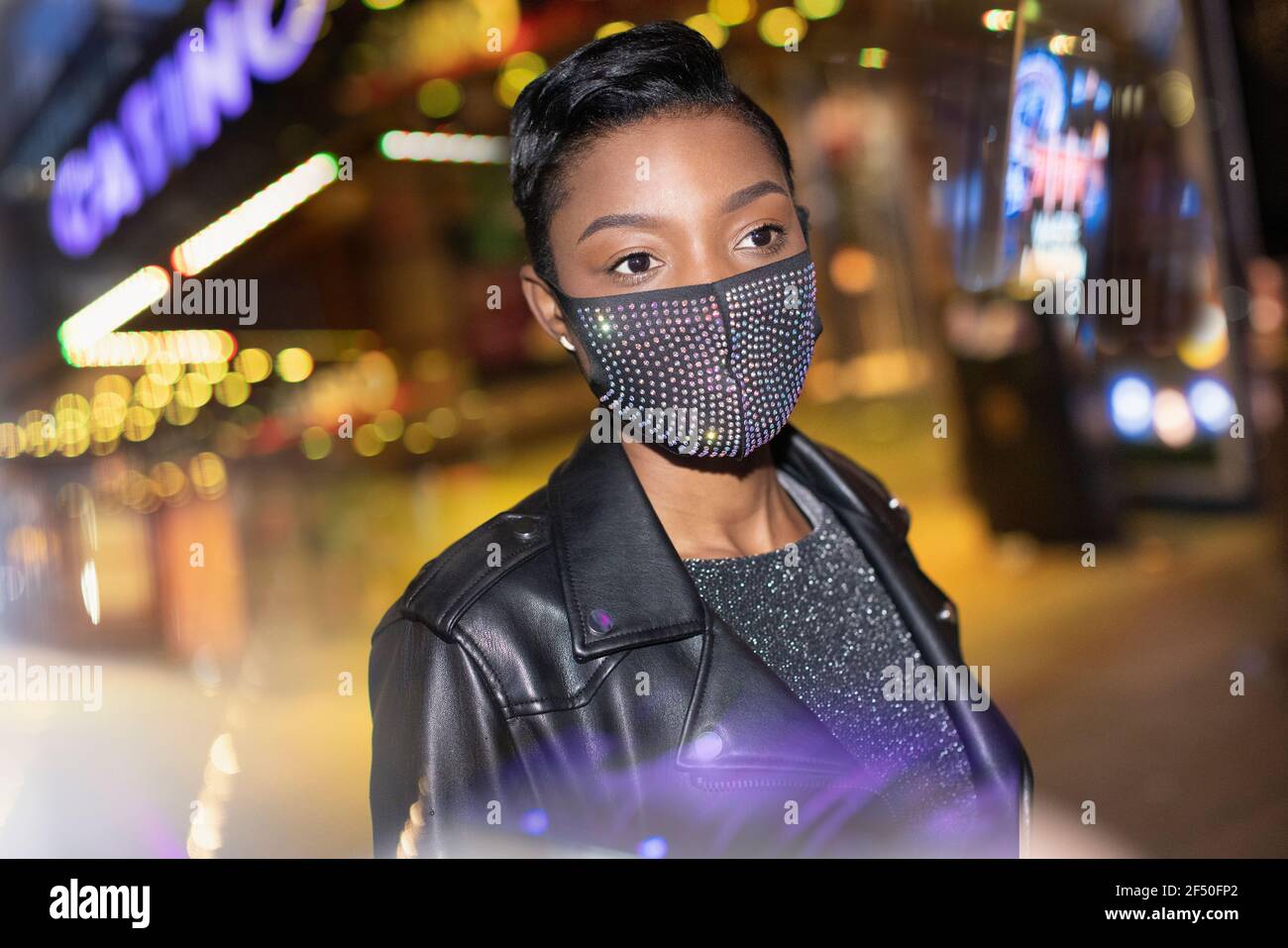 Giovane donna in maschera scintillante in città con luci a. notte Foto Stock