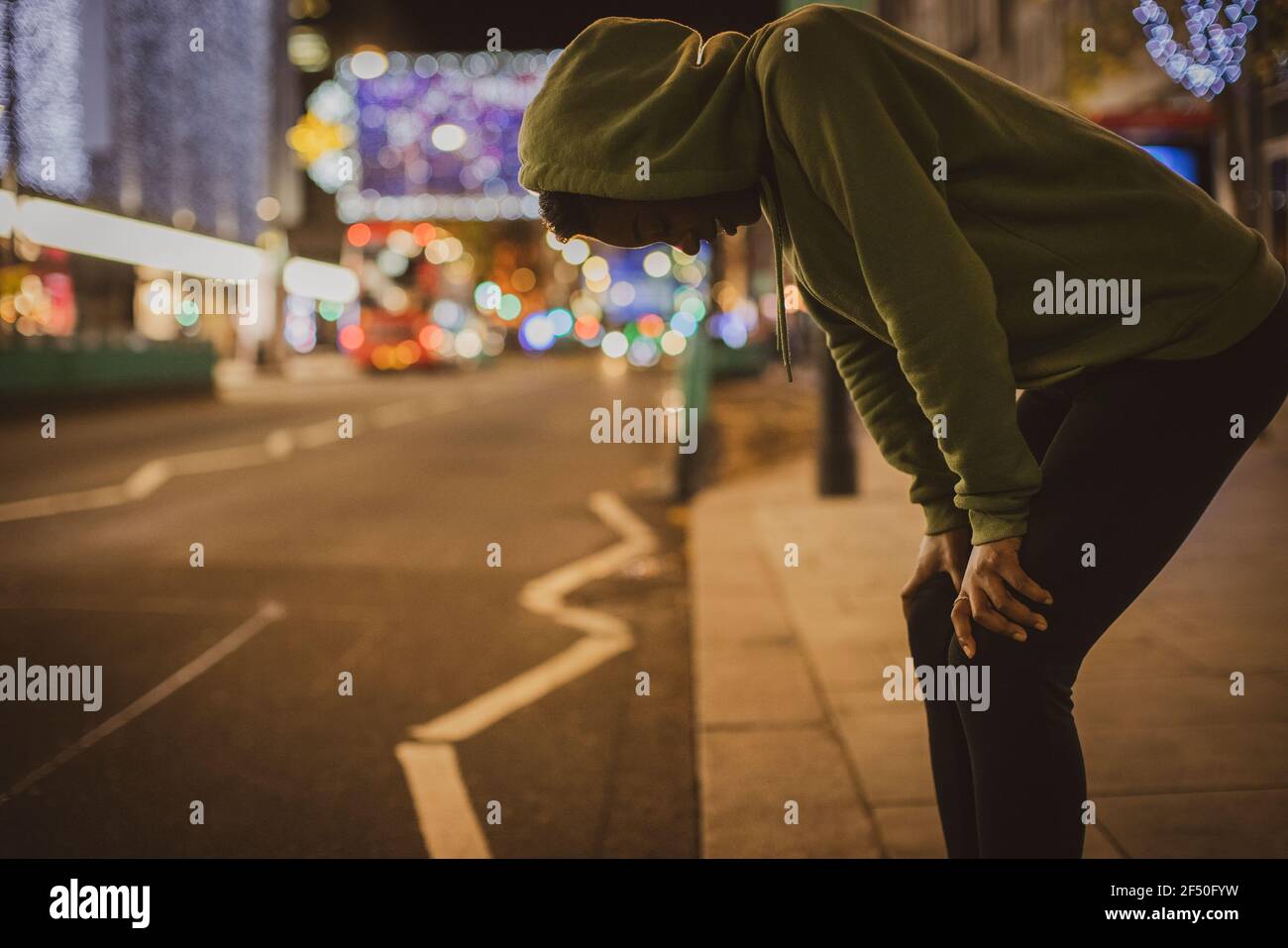 Giovane runner femminile che riposa con le mani sulle ginocchia della città strada di notte Foto Stock