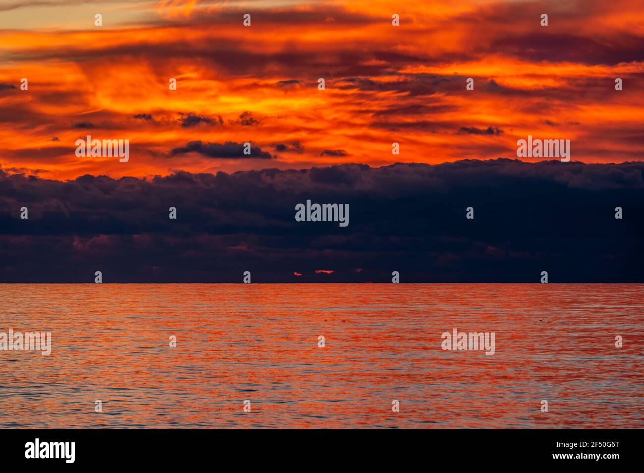 Glorioso tramonto sul mare con nuvole scure sul orizzonte e riflessi rossi sull'acqua increspata Foto Stock