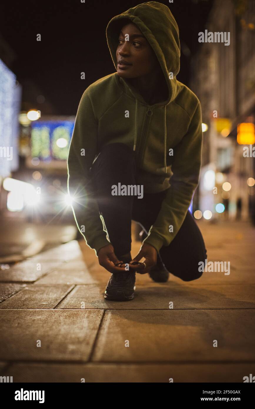 Giovane runner che legano la scarpa sul marciapiede della città di notte Foto Stock