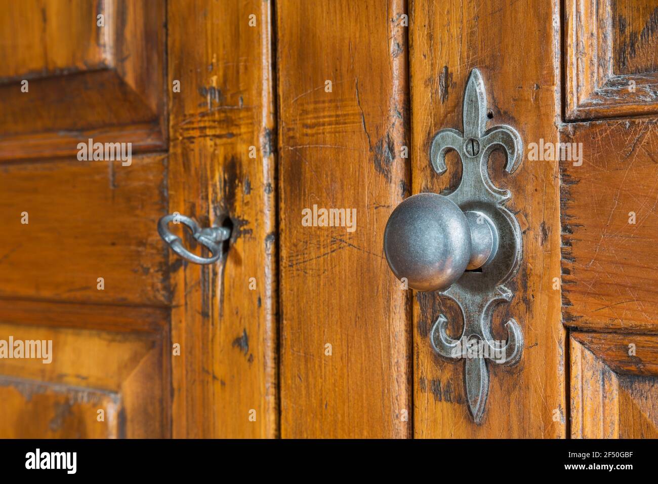 Primo piano di un antico pomolo per portiere con piastra Fleur-de-Lys e chiave in tombino su antico armadio in camera al piano superiore all'interno di una vecchia casa del 1735 Foto Stock