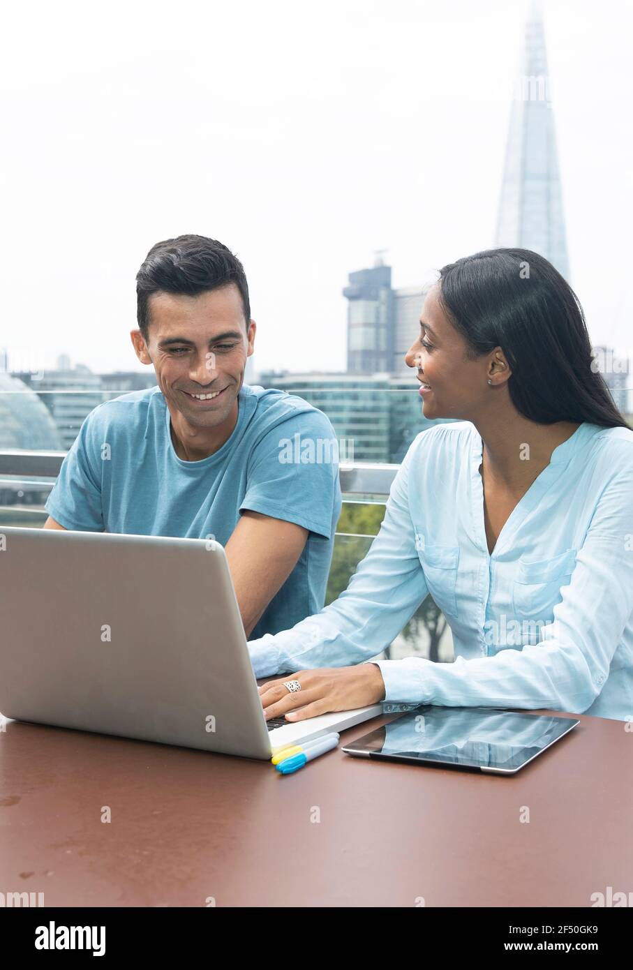 Sorridenti uomini d'affari che lavorano con un computer portatile sul balcone urbano, Londra, Regno Unito Foto Stock