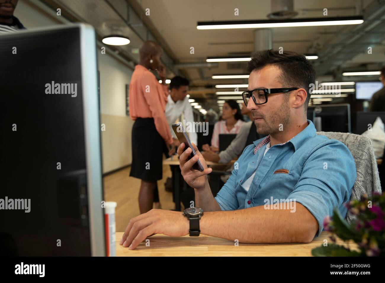 Uomo d'affari che usa lo smartphone al computer in un ufficio open space Foto Stock