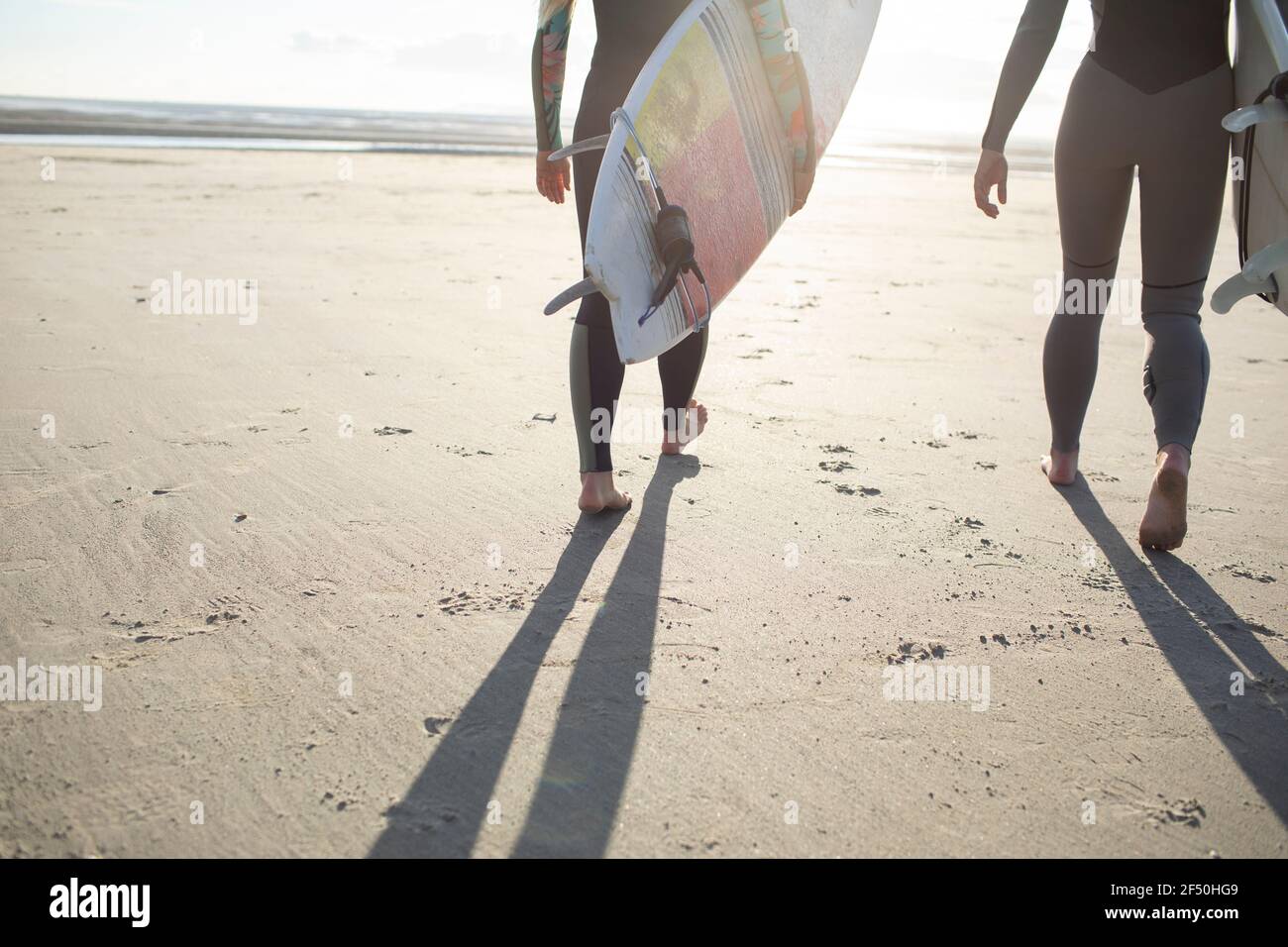 Surfisti femminili che portano tavole da surf sulla spiaggia di sabbia soleggiata Foto Stock