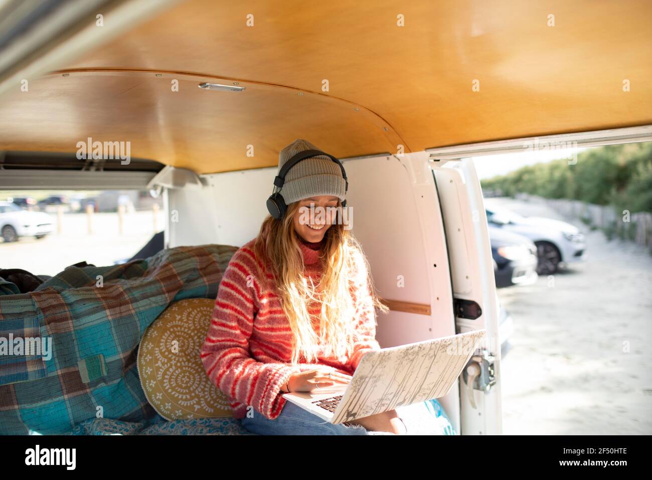 Felice giovane donna che usa le cuffie e il computer portatile in un camper soleggiato furgone Foto Stock
