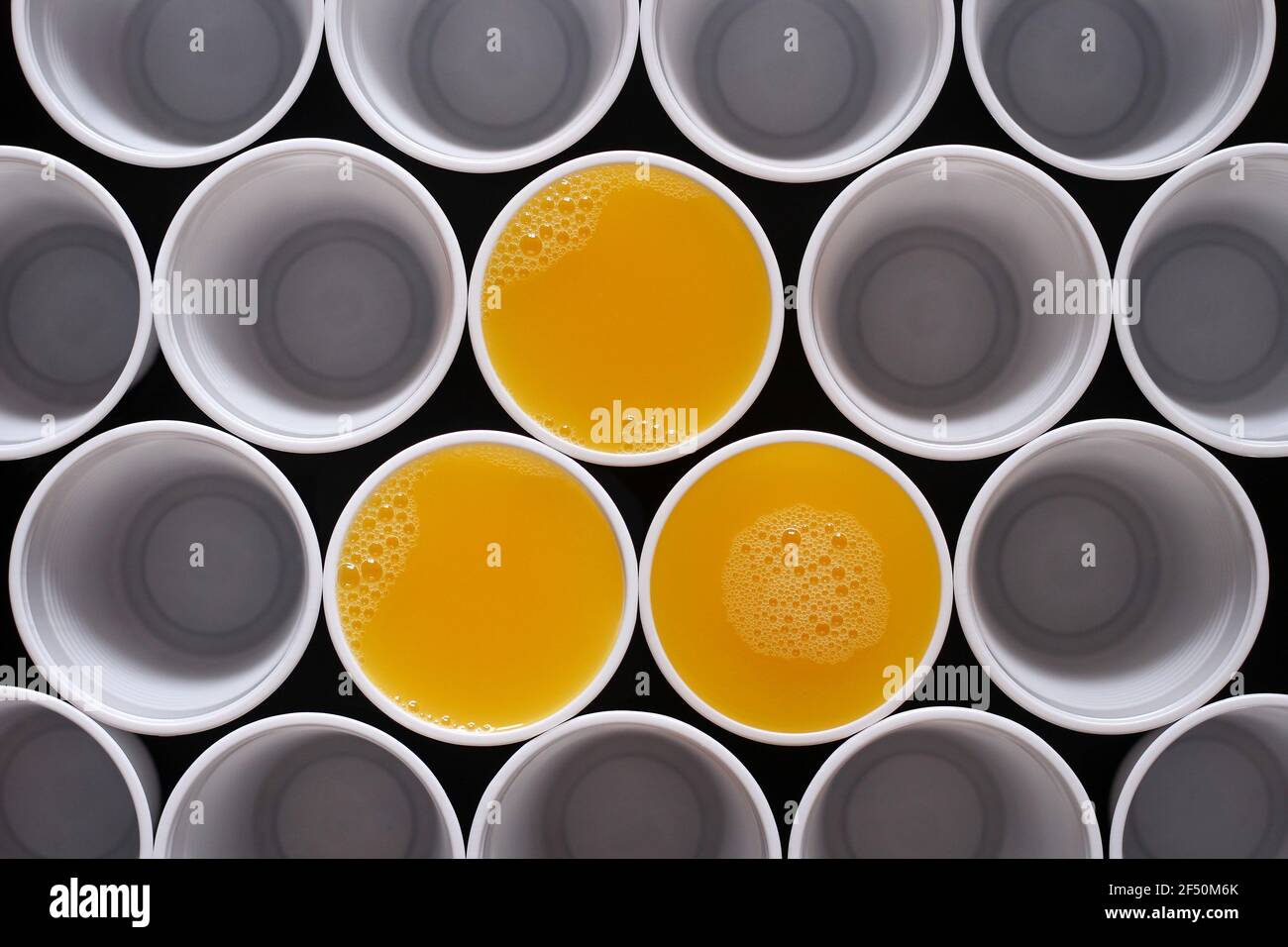Tre tazze monouso in plastica riempite di succo d'arancia, tra le tante altre, viste dall'alto Foto Stock