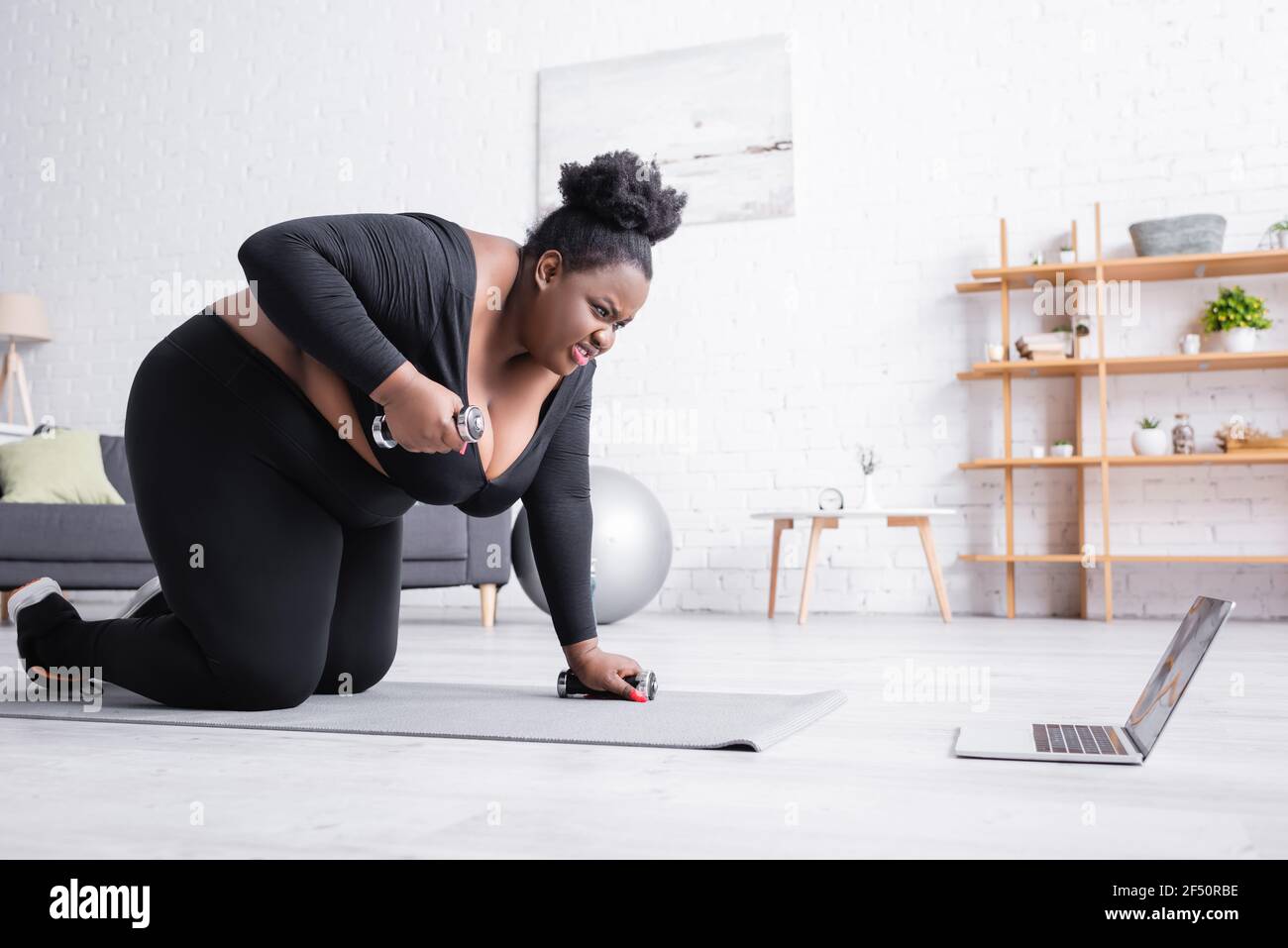 tese african american più taglia donna in abbigliamento sportivo con esercizio dumbbells e guardando un computer portatile Foto Stock