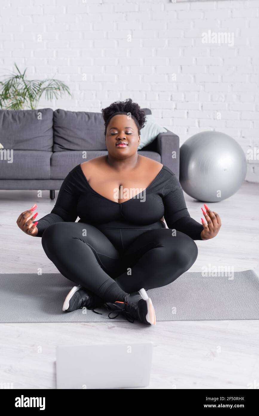 donna afroamericana più taglia in abbigliamento sportivo seduto in yoga  mettiti in posa vicino al computer portatile nel soggiorno Foto stock -  Alamy