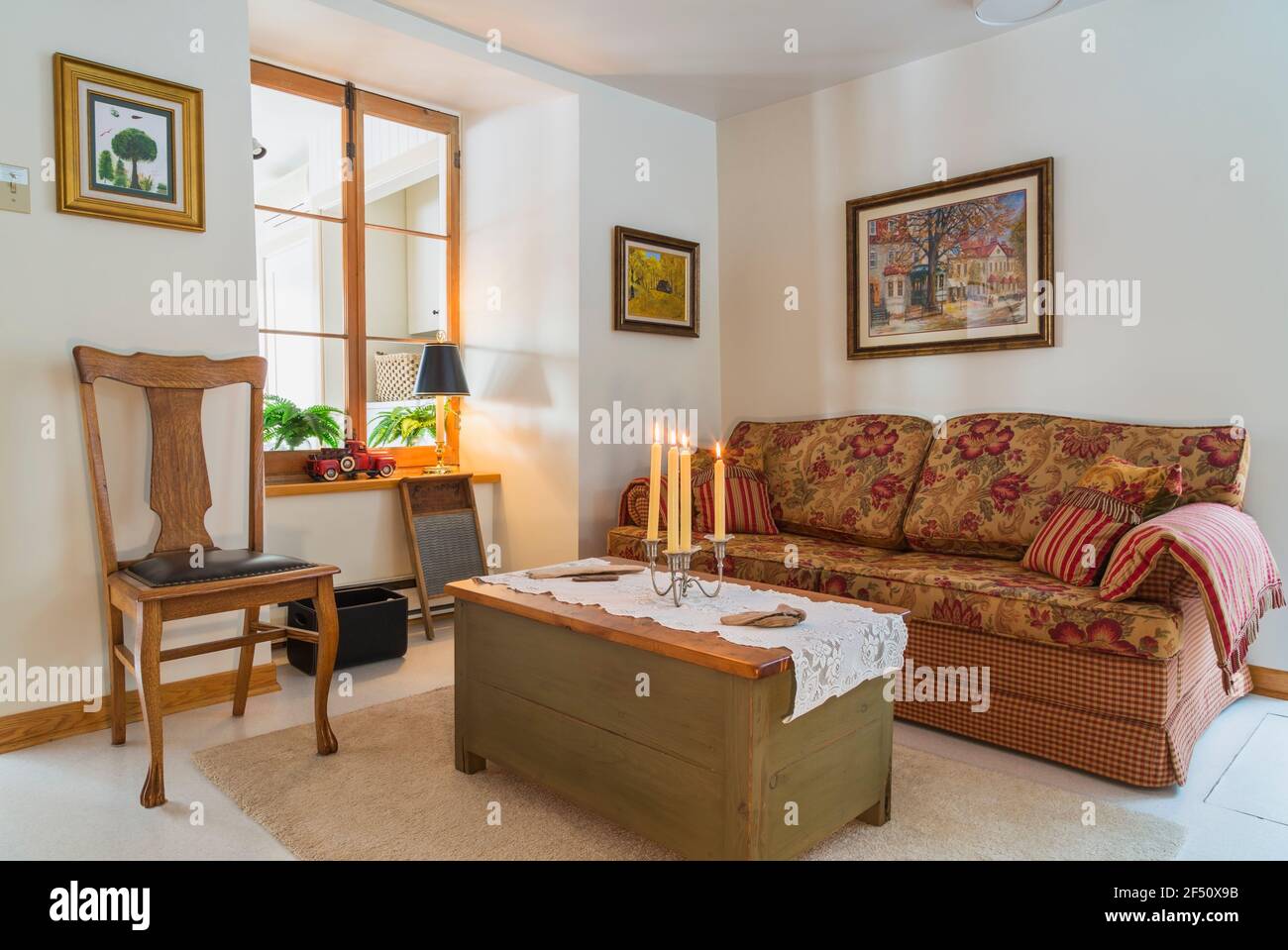 Divano letto a scacchi rosso, beige, grigio con seduta e cuscini in fiore, tavolino da caffè in legno e seggiolone con sedile in pelle nera rivettata Foto Stock