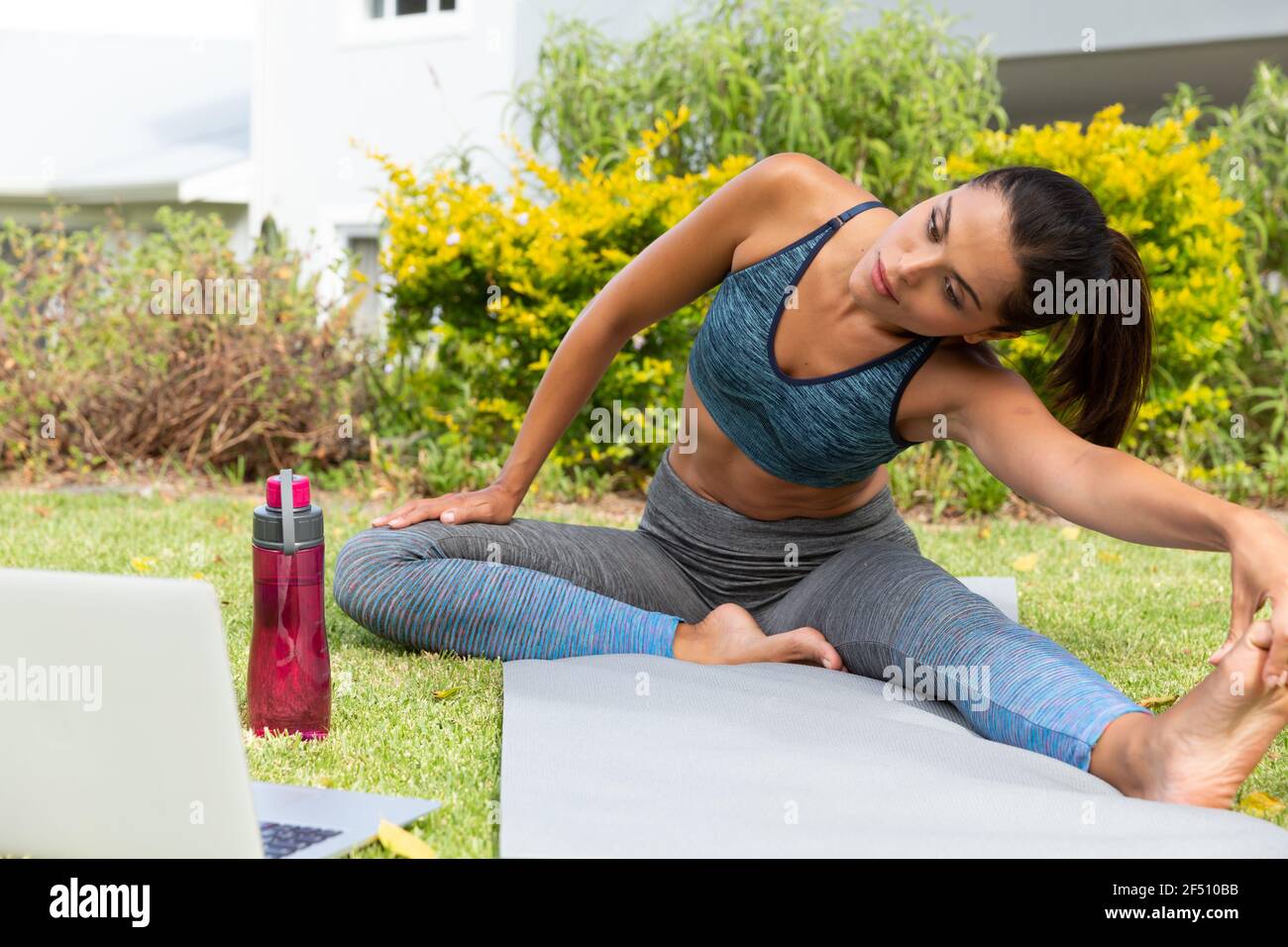 Donna caucasica che pratica yoga e utilizza il computer portatile in giardino Foto Stock
