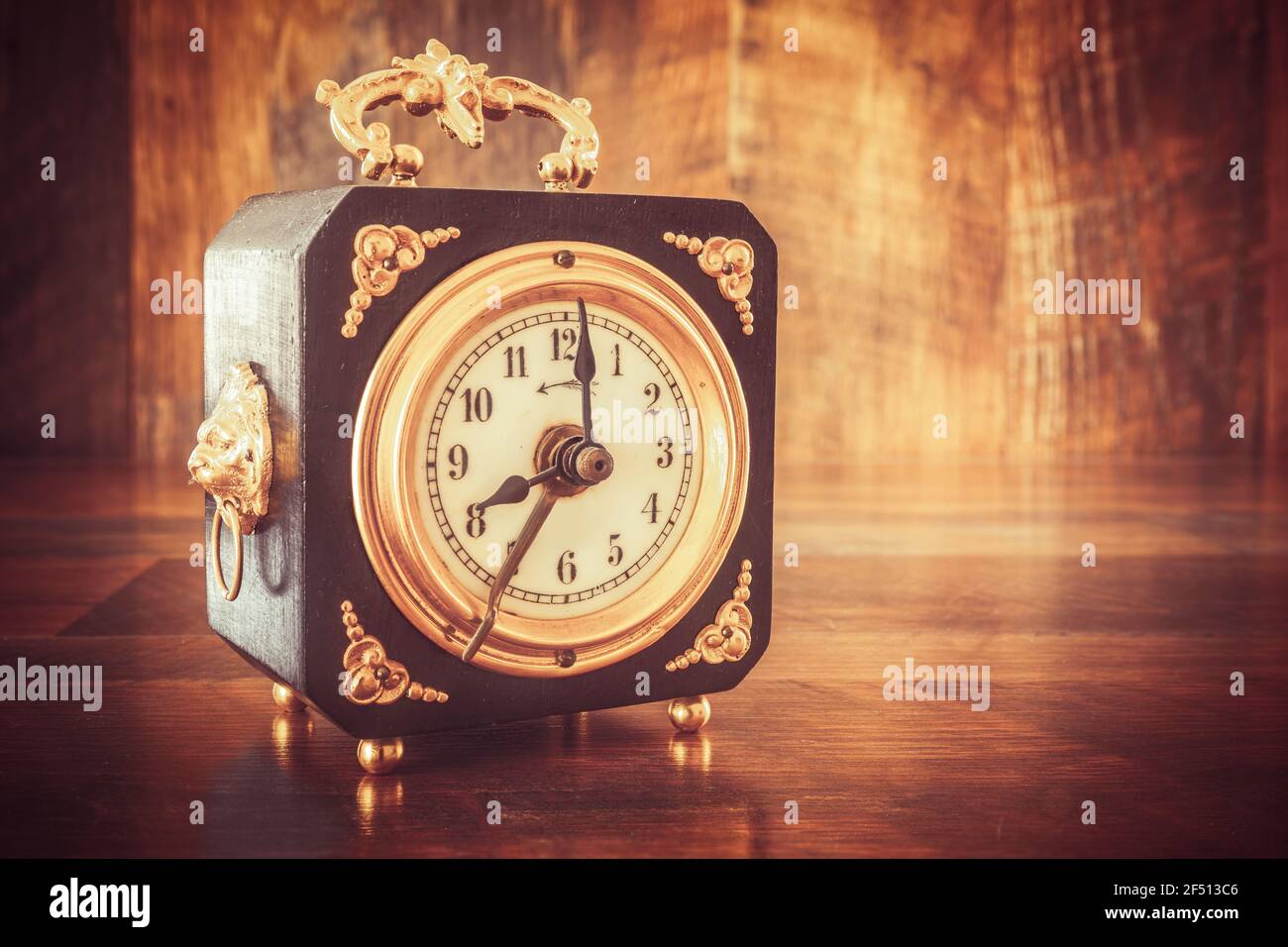 Vecchio orologio in legno con applicazioni in oro, che mostra le ore 8 su un tavolo di legno Foto Stock