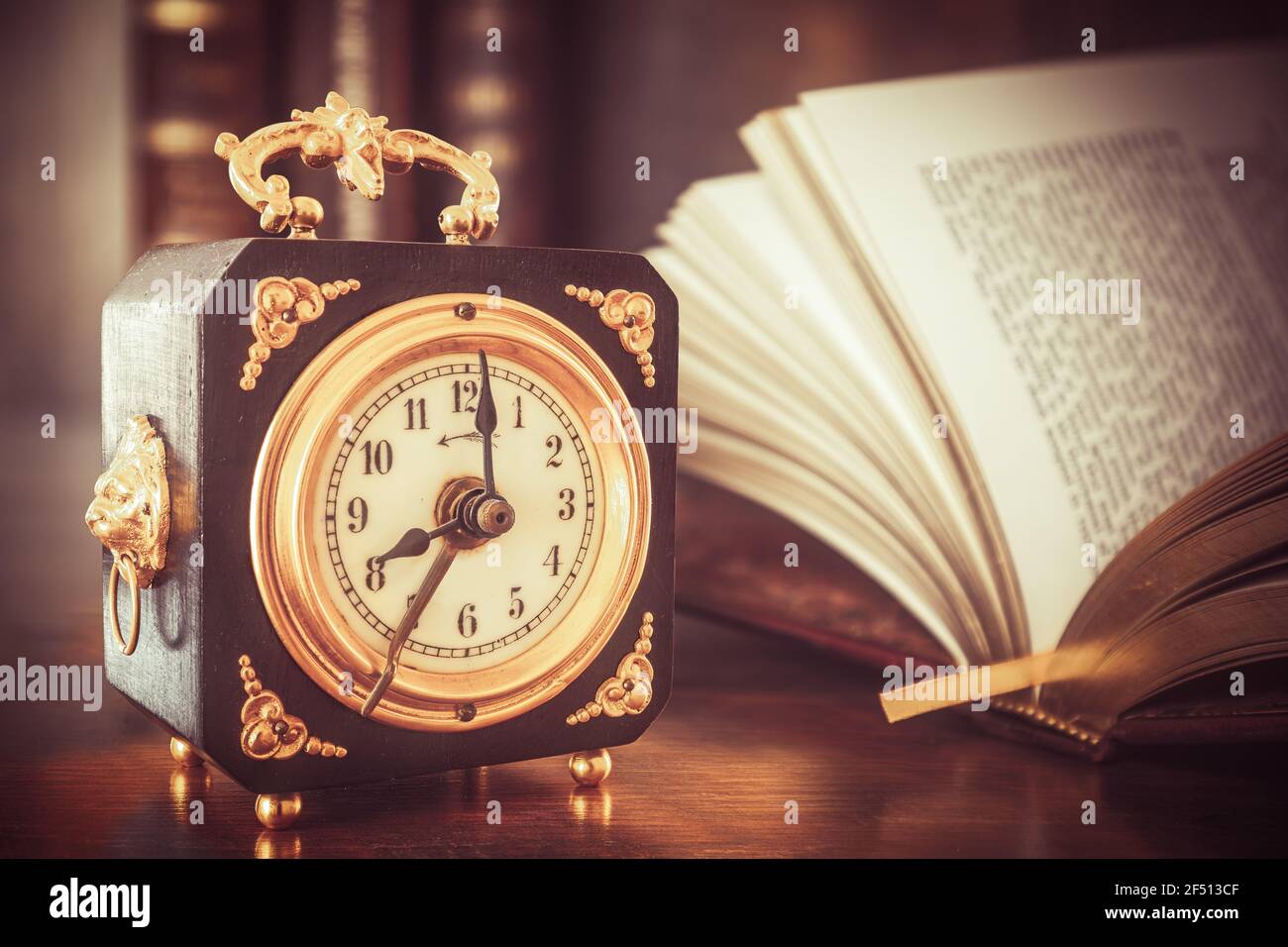 Vecchio orologio in legno con applicazioni in oro, che mostra le ore 8 su un tavolo di legno con libri sullo sfondo Foto Stock
