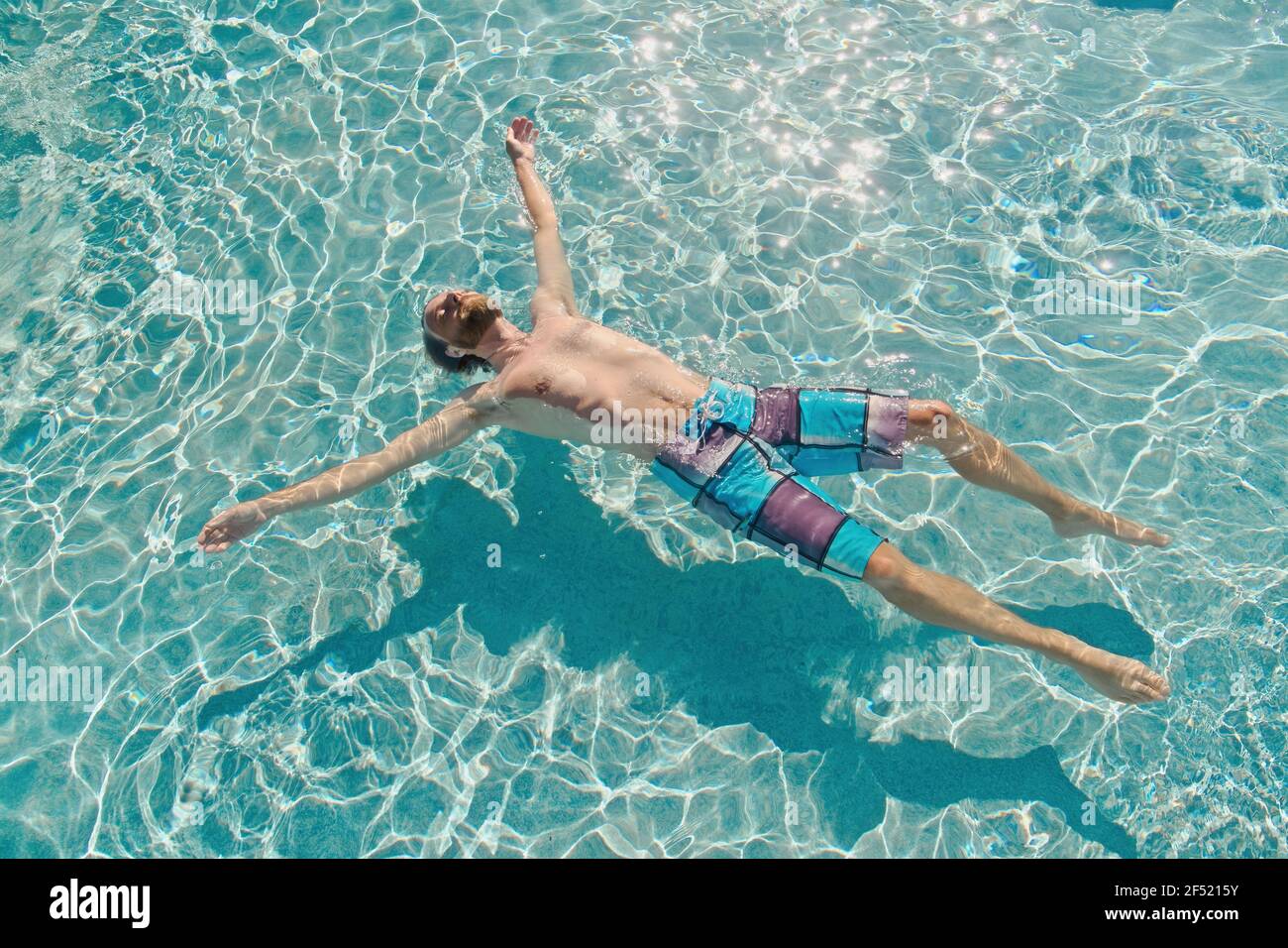 Uomo che galleggia sull'acqua blu in trazione con le braccia tese ampio sotto la luce diretta del sole Foto Stock