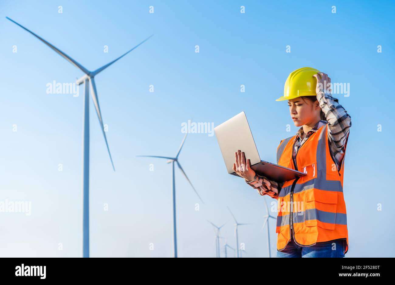 giovane ha sottolineato femmina ingegnere che ha problemi a lavorare con il portatile computer contro l'azienda agricola di turbine eoliche Foto Stock