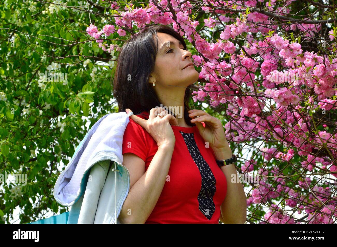 Ritratto di 45 anni Donna russa che sniffing sakura ramo sullo sfondo di fiore mela albero in primavera. Foto Stock