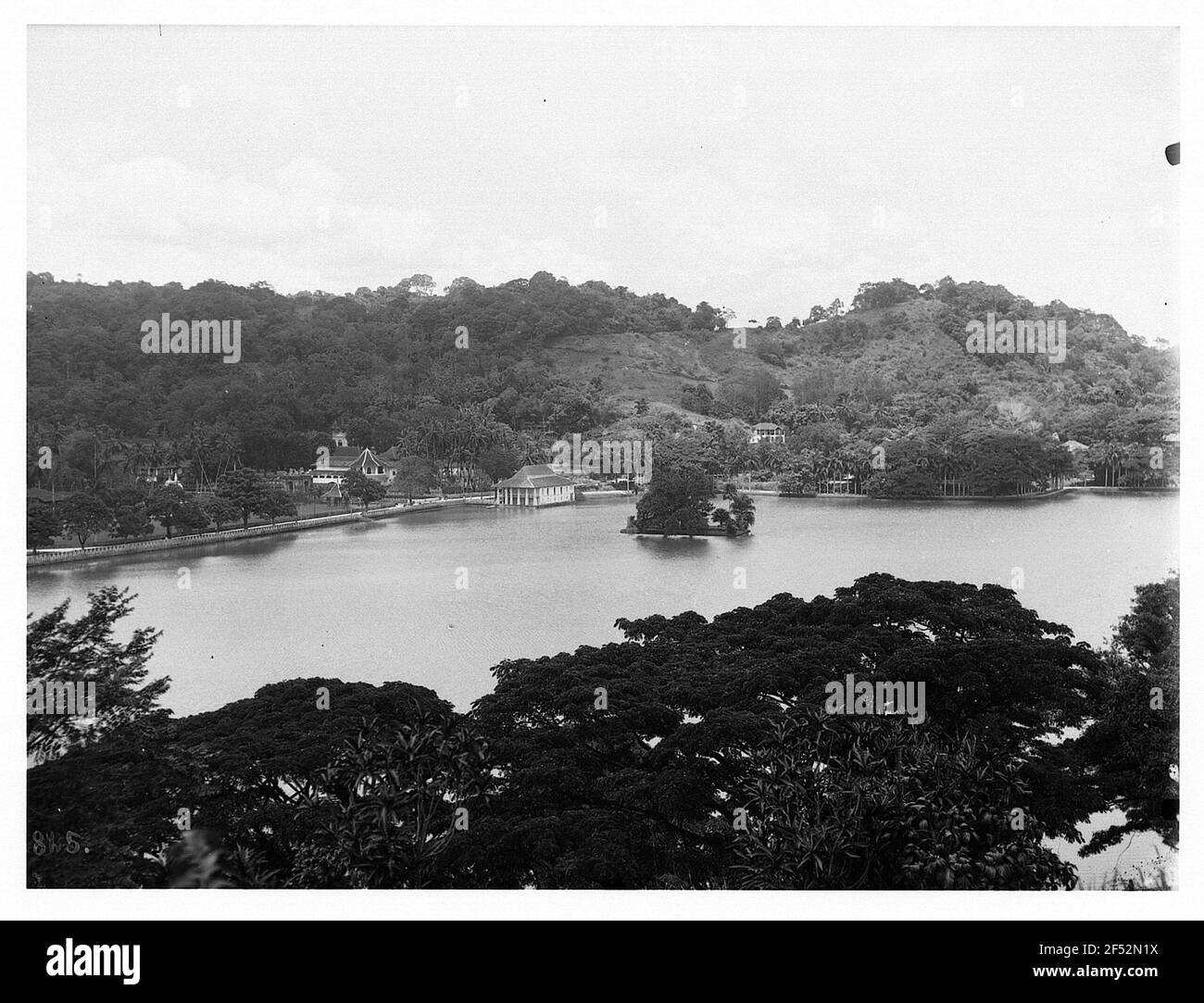 Colombo, Sri Lanka. Vista su un parco marittimo con vegetazione lussureggiante e baia con isolotto ben artificiale contro la zona costiera popolata Foto Stock
