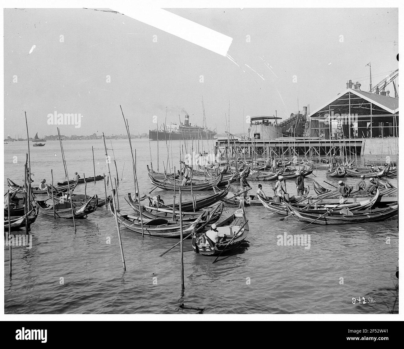Rangonn, Birmania. Attracco barca nel porto con gli uomini nativi in gondola denti, sullo sfondo Hap-Sea passeggero vaporiera del Hapag (forse Cleveland) Foto Stock