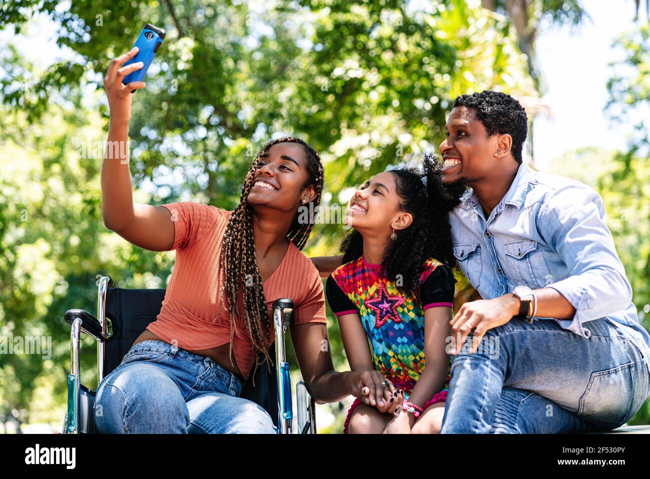 Donna in sedia a rotelle che prende un selfie con la sua famiglia. Foto Stock