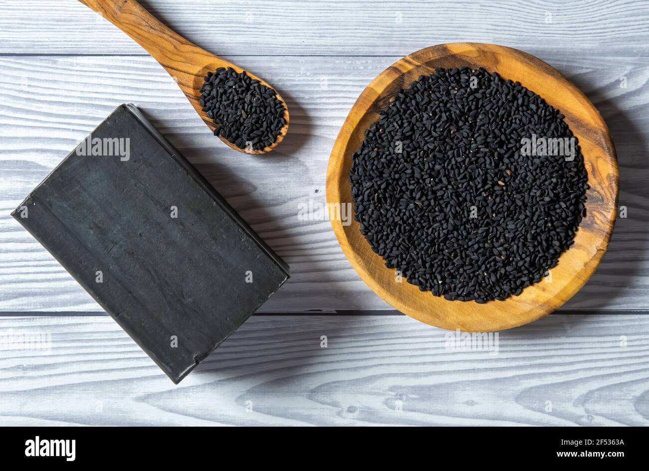 Nigella sativa semi vista dall'alto, in un piatto di legno e cucchiaio di legno. Su un tavolo di legno grigio. Foto Stock