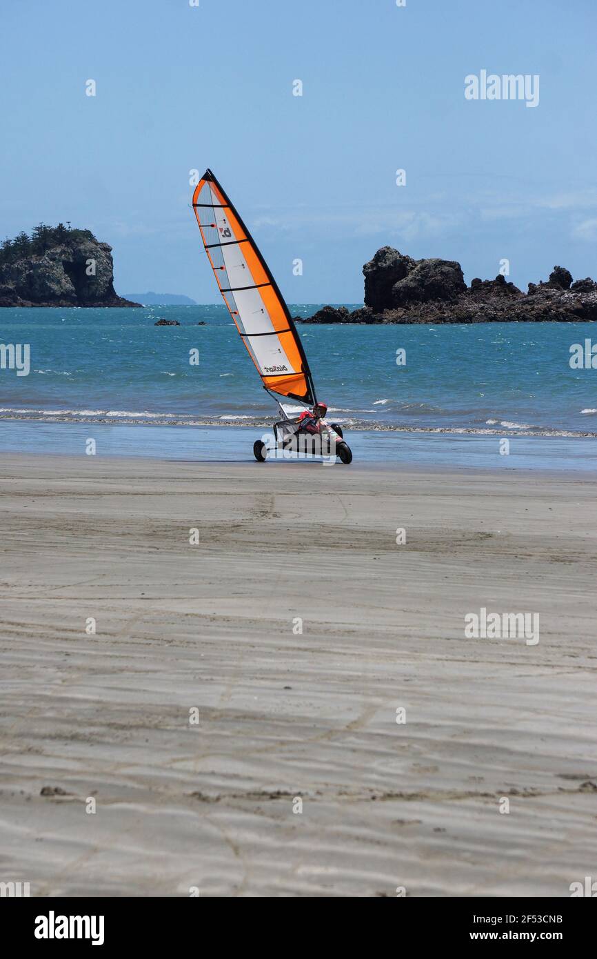 Uno yacht blokart o Land con una vela arancione che corre sulla sabbia contro uno splendido sfondo tropicale a Queensland, Australia. Foto Stock