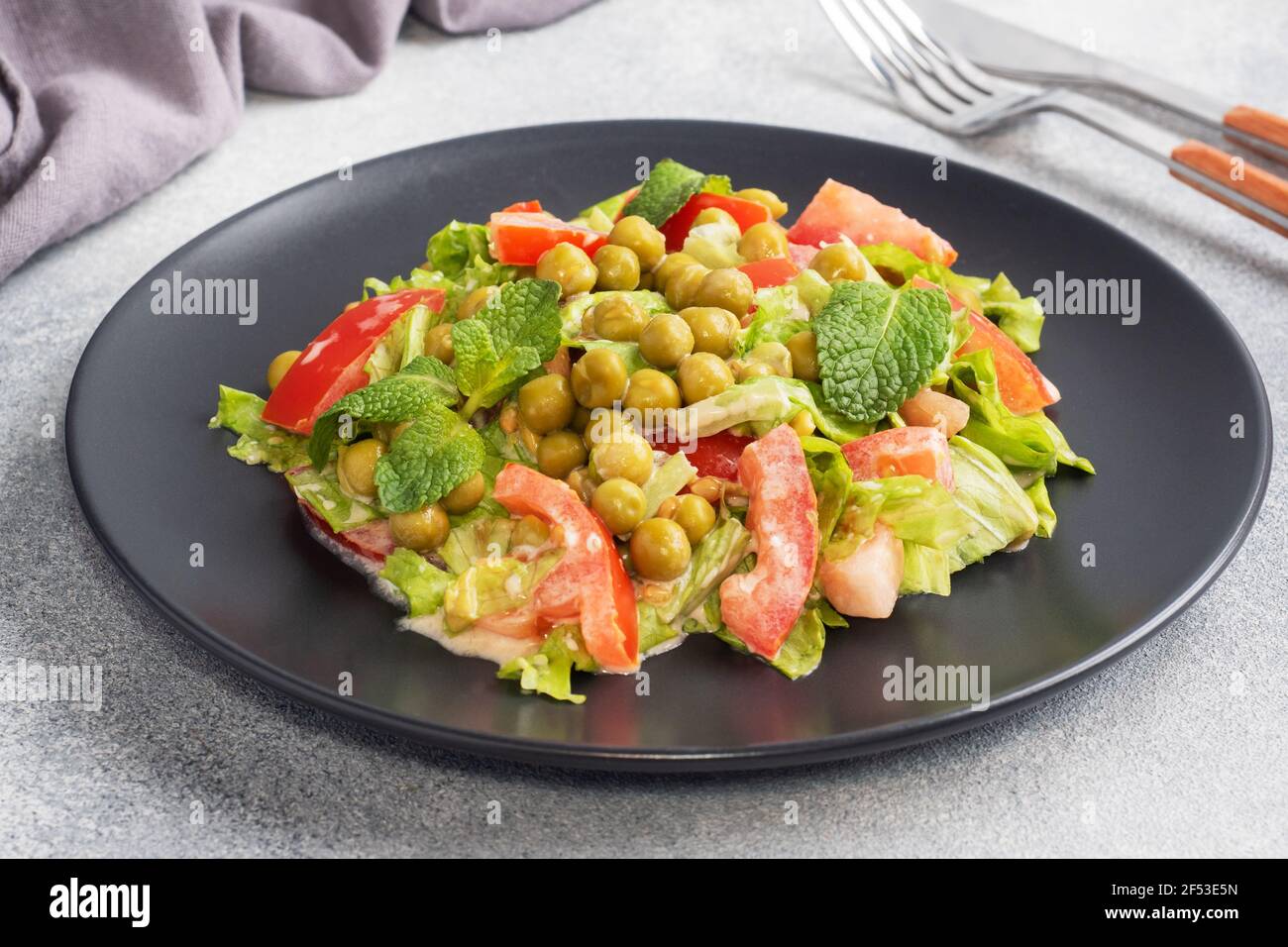 Insalata di foglie di pomodoro verde e piselli in scatola conditi con salsa  su un piatto nero. Insalata di dieta fresca di primavera Foto stock - Alamy