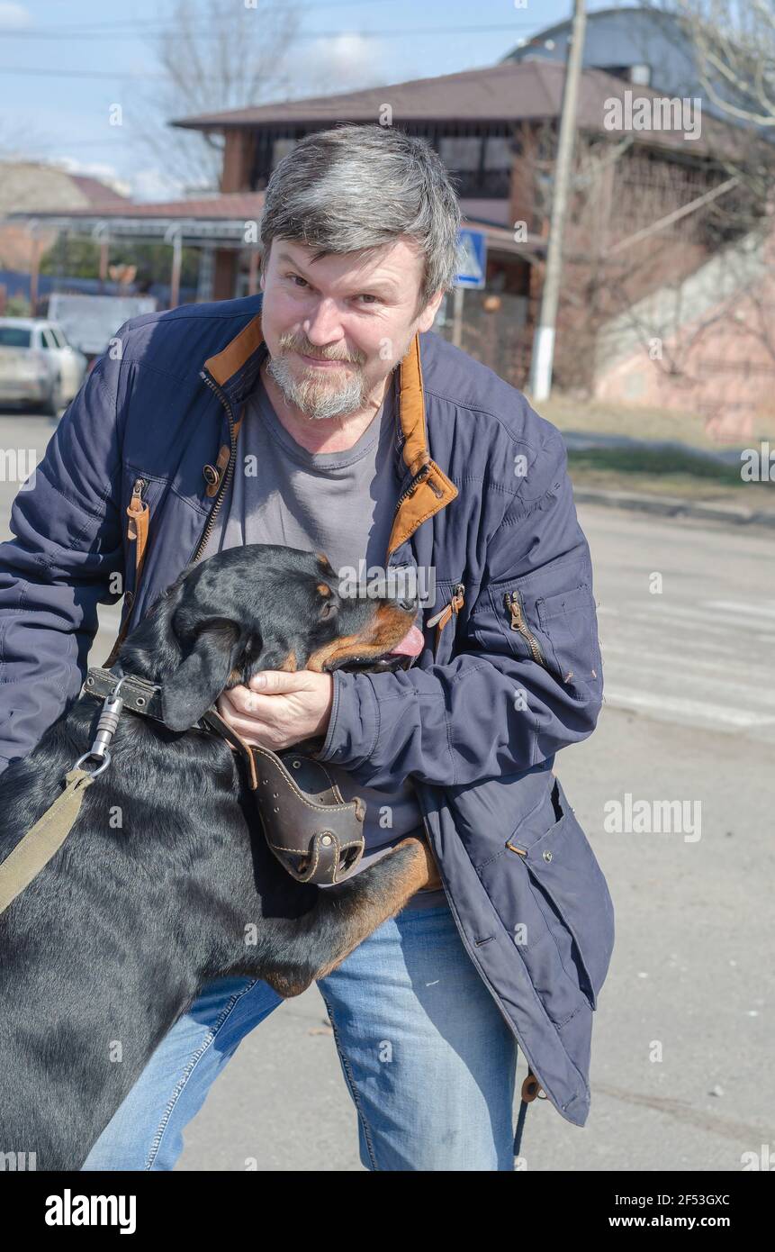 Il tanto atteso incontro del cane e del proprietario dopo una lunga separazione. Un uomo di mezza età che grava abbracca una femmina Rottweiler nel mezzo della primavera Foto Stock