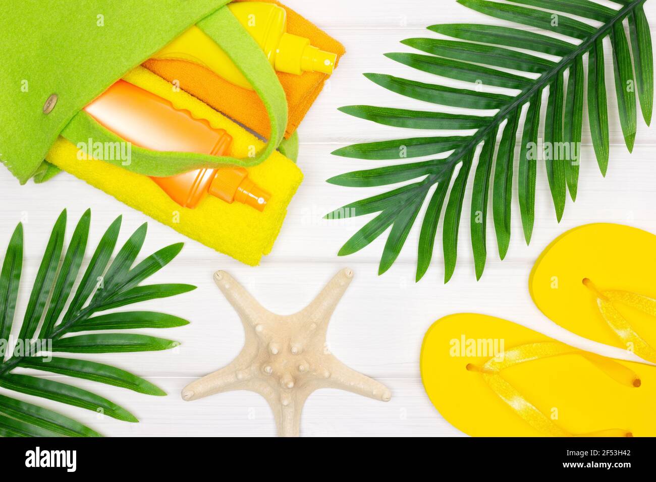 Estate mare spiaggia vacanza composizione creativa. Borsa con asciugamani e crema solare, sandali infradito, stelle marine, foglie di palma tropicali Foto Stock
