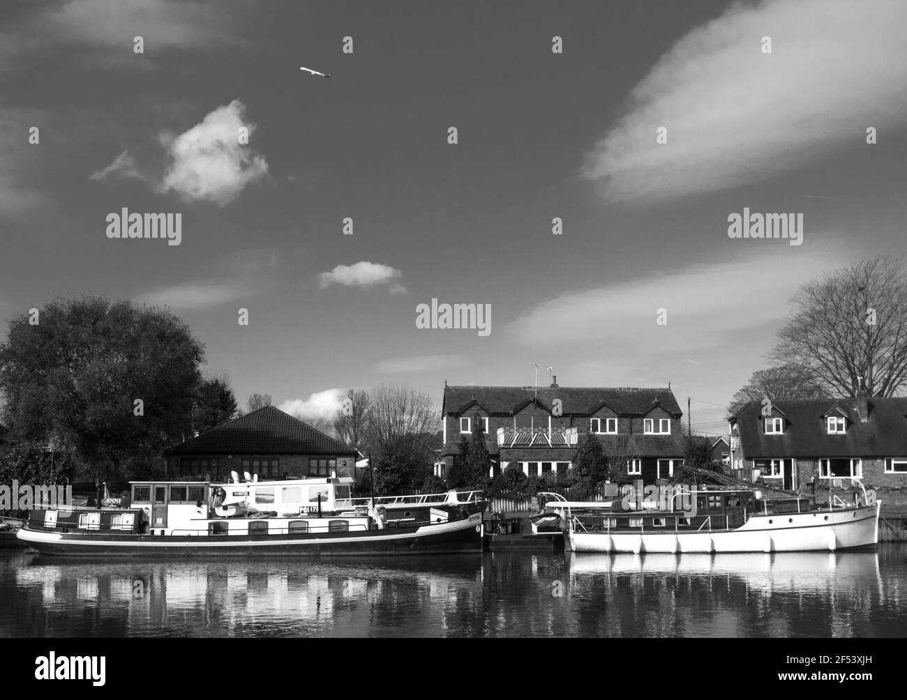 Barche ormeggiate sul Tamigi a Staines-upon-Thames, Surrey, Regno Unito come un jet passa sopra. B&N. Foto Stock
