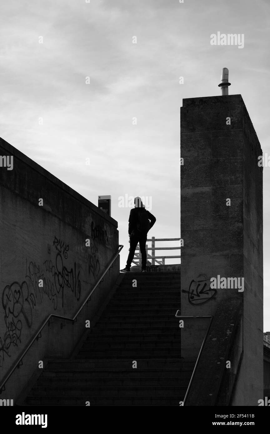 Una silhouette bianca e nera di un uomo solitario in piedi, mano sull'anca, in cima a una scala esterna in cemento con graffiti sulle pareti Foto Stock