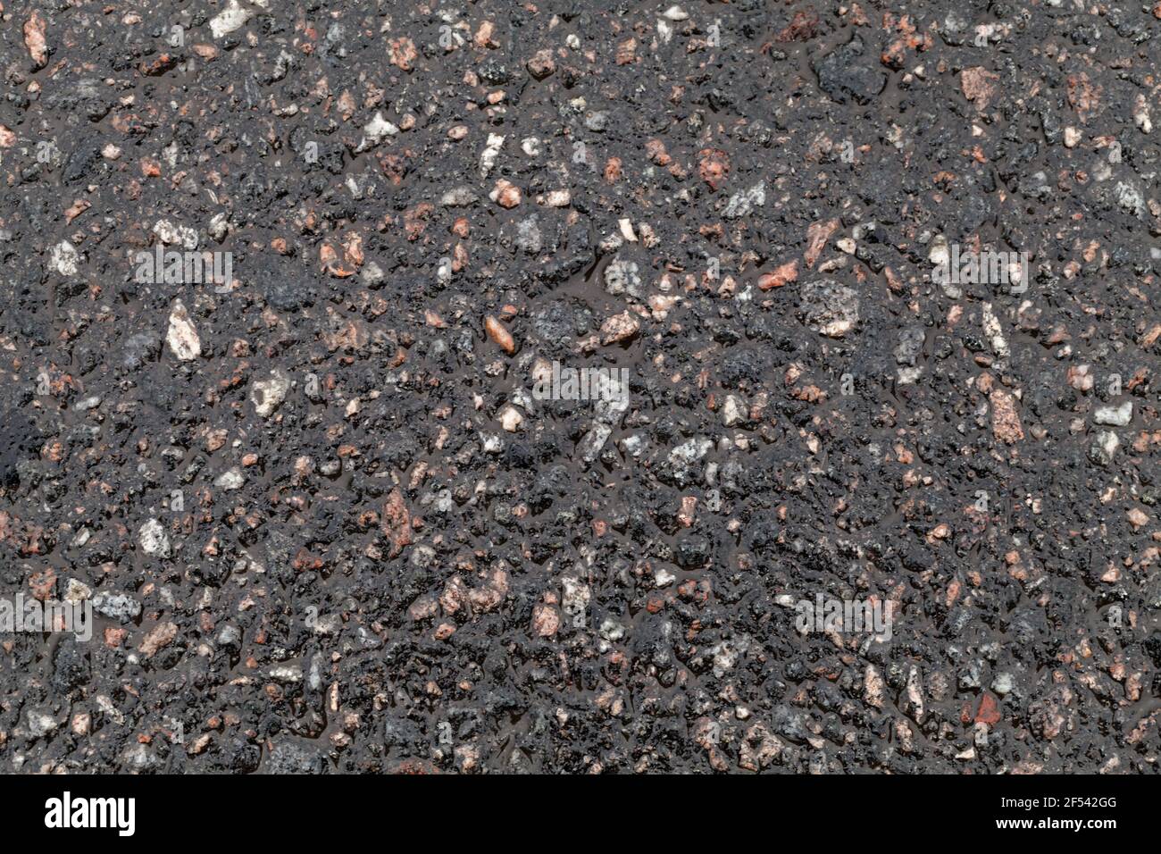 Superficie stradale bagnata. Texture asfaltata, pavimentazione stradale scura costituita da roccia frantumata mescolata con catrame. Foto di sfondo Foto Stock