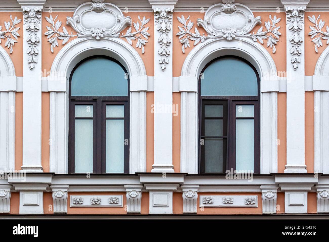 Due finestre ad arco con cornici in legno marrone contro una parete rosa con stucco bianco. Da una serie di finestre di San Pietroburgo. Foto Stock