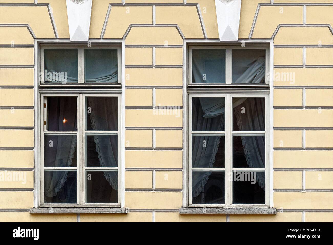 Due finestre rettangolari con vecchie cornici in legno e tende contro una parete di stucco giallo. Dalle finestre della serie di San Pietroburgo. Foto Stock