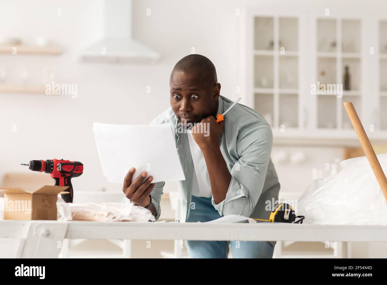 Problemi con il nuovo montaggio di mobili. Scioccato uomo afro-americano che legge le istruzioni a casa Foto Stock