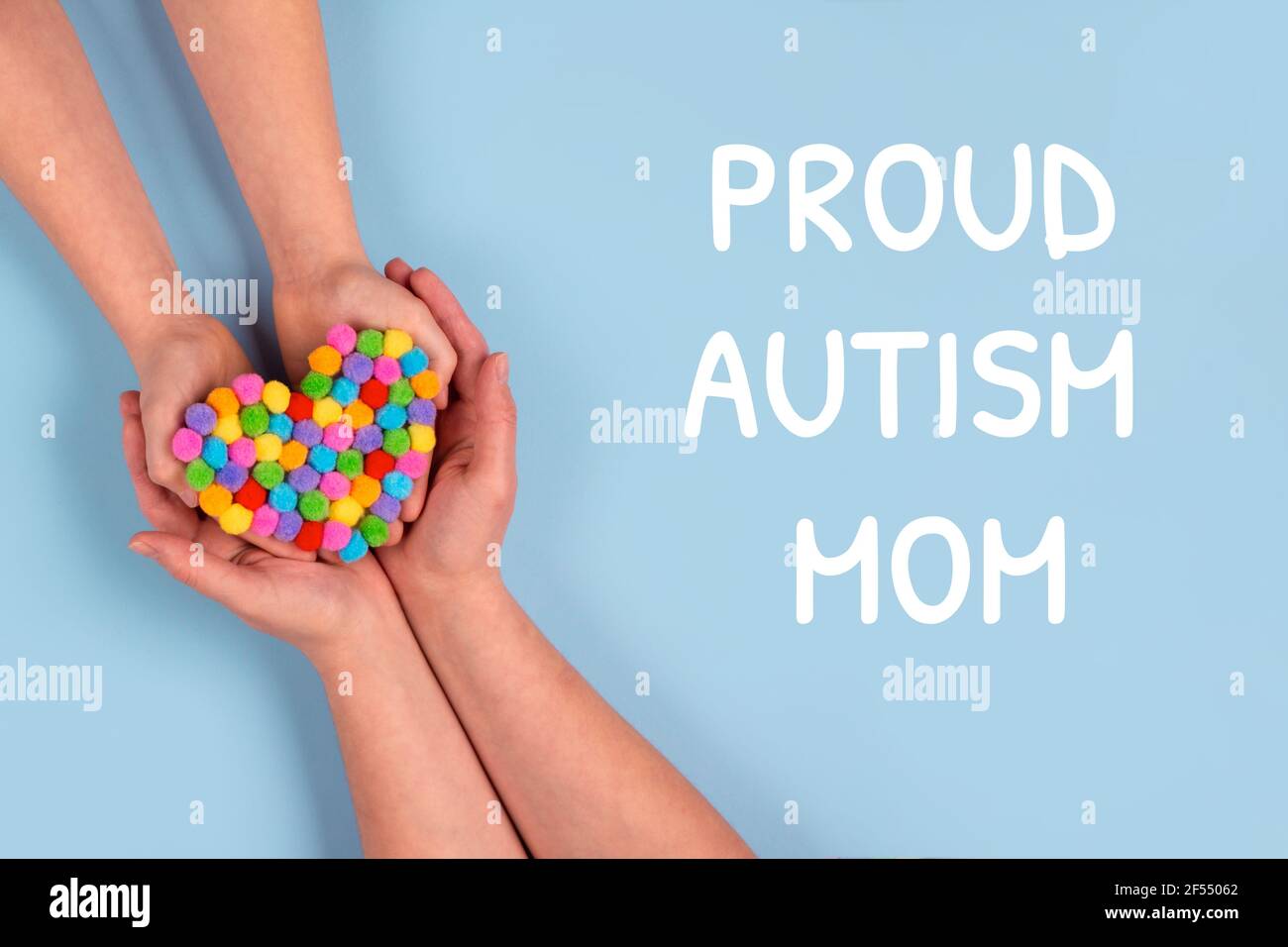 Orgoglioso autismo mamma e mondo Autismo consapevolezza giorno concetto - mani autistiche del bambino supportate dalla madre che tiene il cuore multicolore su sfondo blu Foto Stock